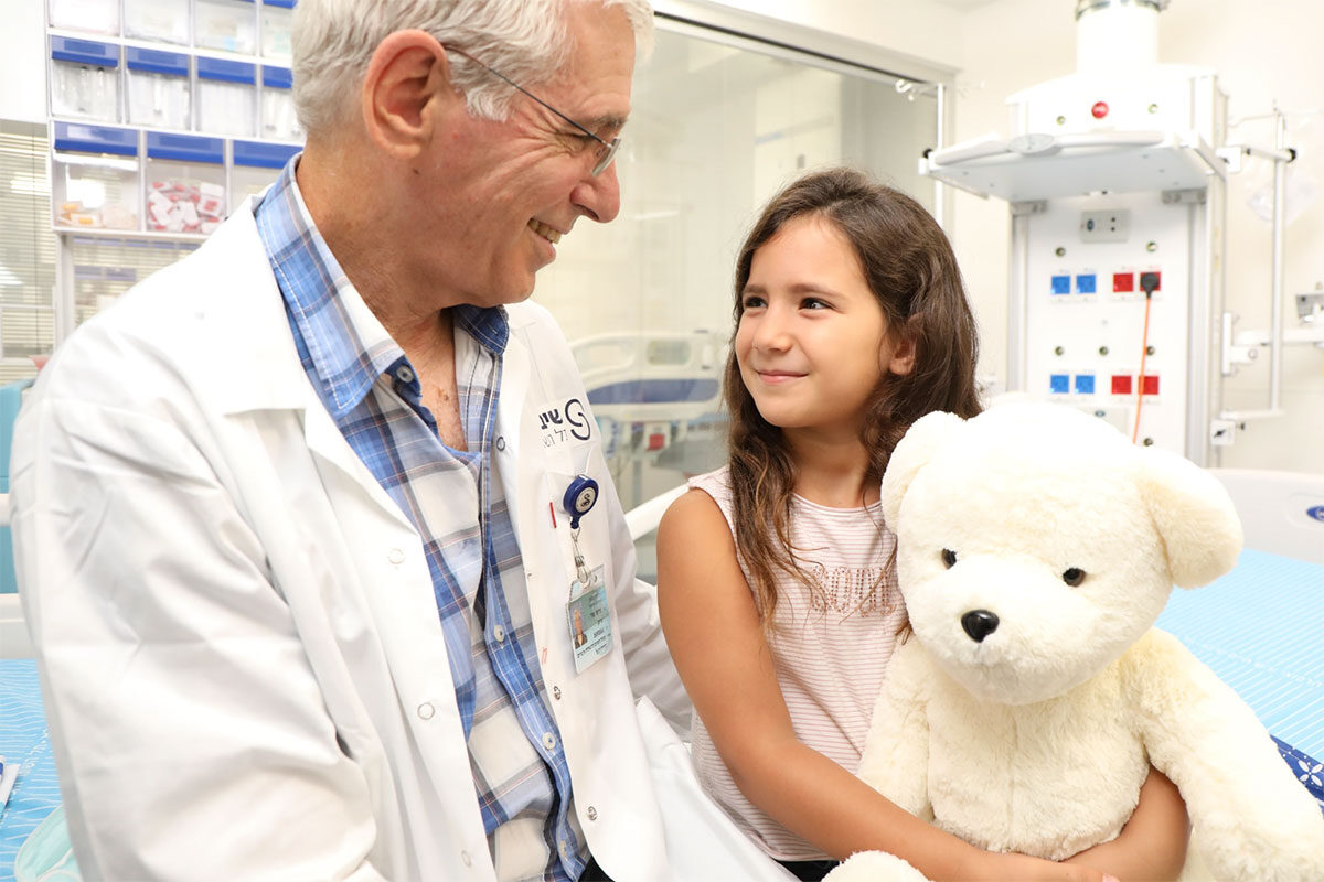 A doctor smiling at a young girl patient, who is holding a teddy bear