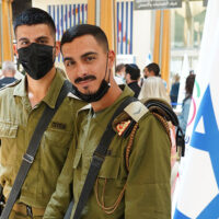 Two IDF soldiers stand next to an Israeli flag