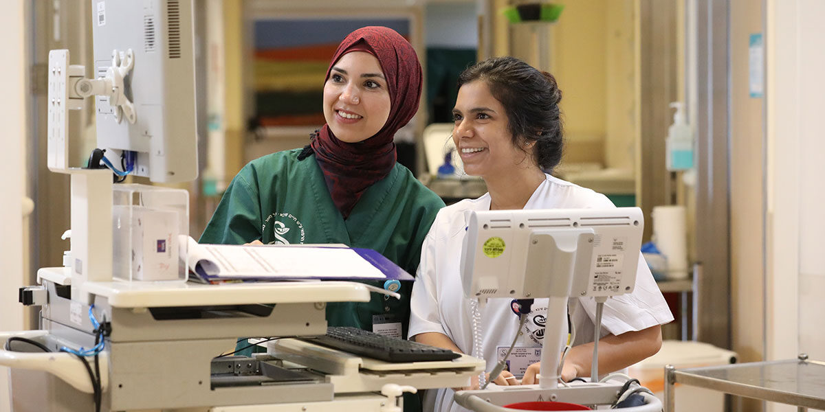 Two female Sheba employees, one wearing a hijab, work together